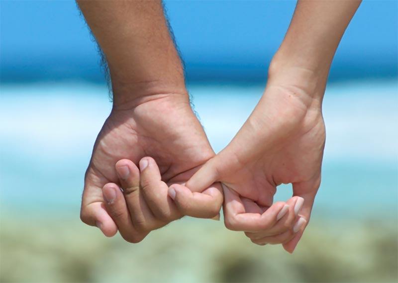 Man and woman holding pinky fingers on beach